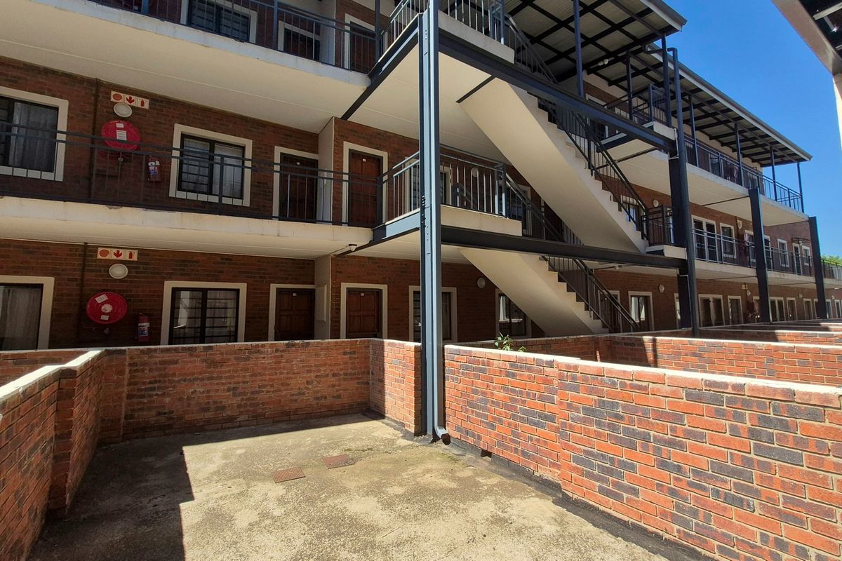 Exterior view of a multi-story apartment complex featuring brick facade, external metal staircases, and private ground-level patio areas.