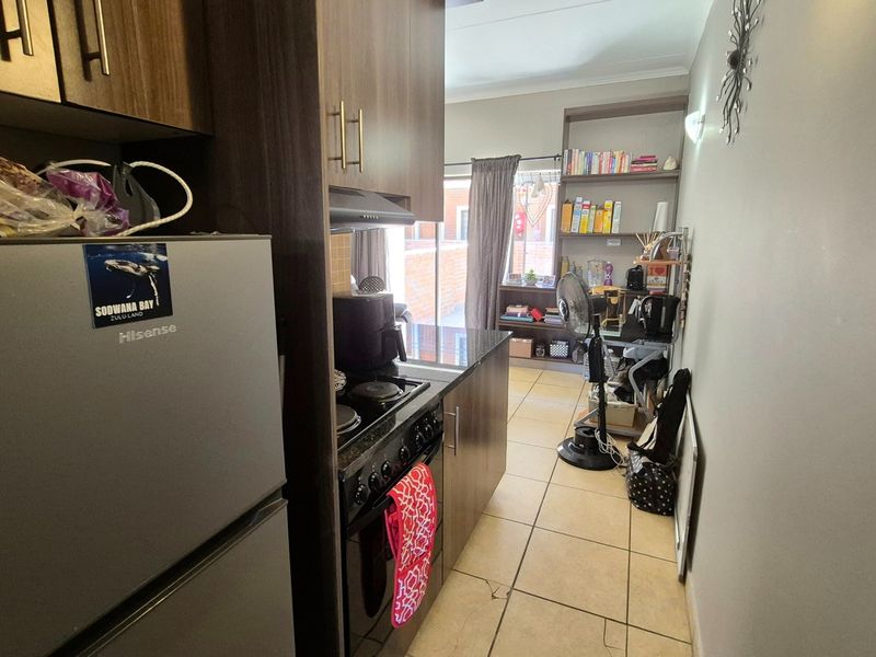 Compact kitchen featuring dark wood cabinetry, built-in oven and hob, extractor fan, and tiled flooring, leading into a small adjacent living area.