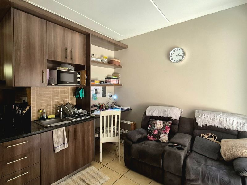 Compact open-plan living area featuring a kitchenette with dark wood cabinetry, laminate countertops, and integrated shelving, seamlessly connected to the living space.