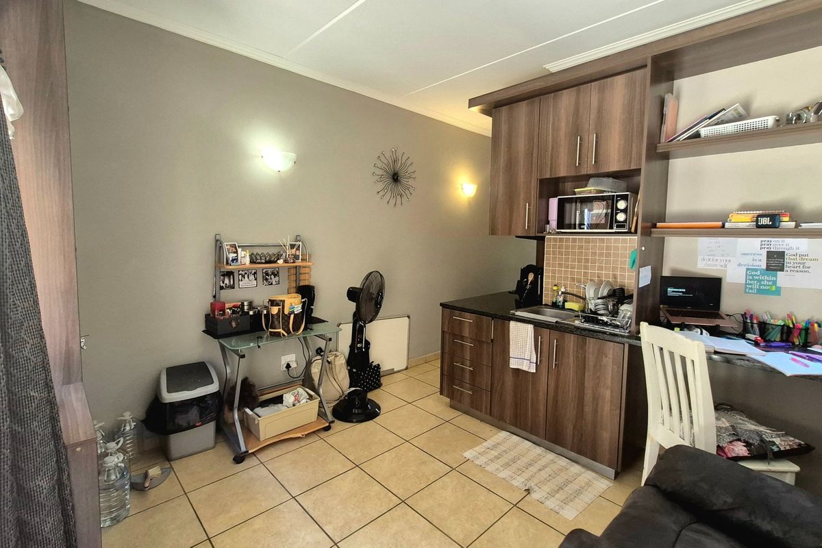 Compact kitchen area featuring wood-finish cabinetry, dark countertops, tiled backsplash, and ceramic floor tiles, integrated into a multi-purpose living space.