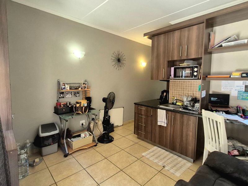 Compact kitchen area featuring wood-finish cabinetry, dark countertops, tiled backsplash, and ceramic floor tiles, integrated into a multi-purpose living space.