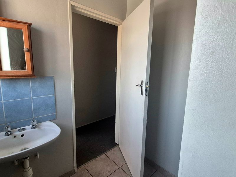 A functional bathroom space featuring a wall-mounted basin with tiled splashback and a wooden medicine cabinet, requiring cosmetic updates.