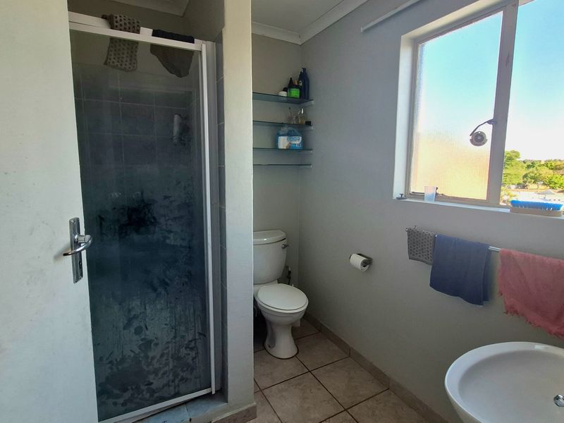 A functional bathroom featuring a shower enclosure, toilet, washbasin, and tiled flooring, with natural light provided by a side window.