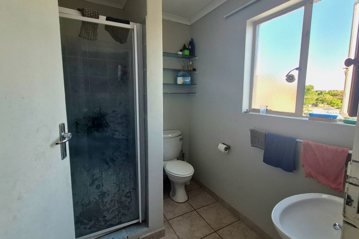 A functional bathroom featuring a shower enclosure, toilet, washbasin, and tiled flooring, with natural light provided by a side window.