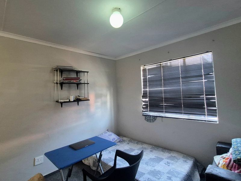 A compact bedroom featuring a window with venetian blinds, standard electrical outlets, and a central ceiling light fixture.
