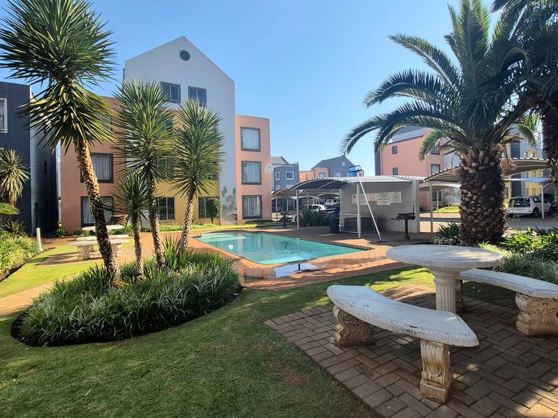 Communal outdoor area featuring a swimming pool, landscaped gardens, and a covered braai facility within the apartment complex grounds.