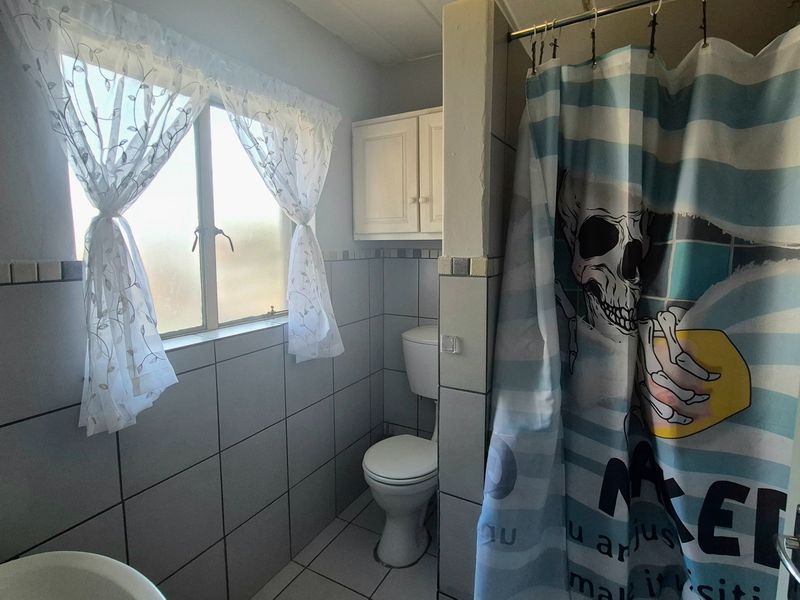 A functional bathroom featuring tiled walls and flooring, a standard toilet, and a shower area with a wall-mounted storage cabinet.