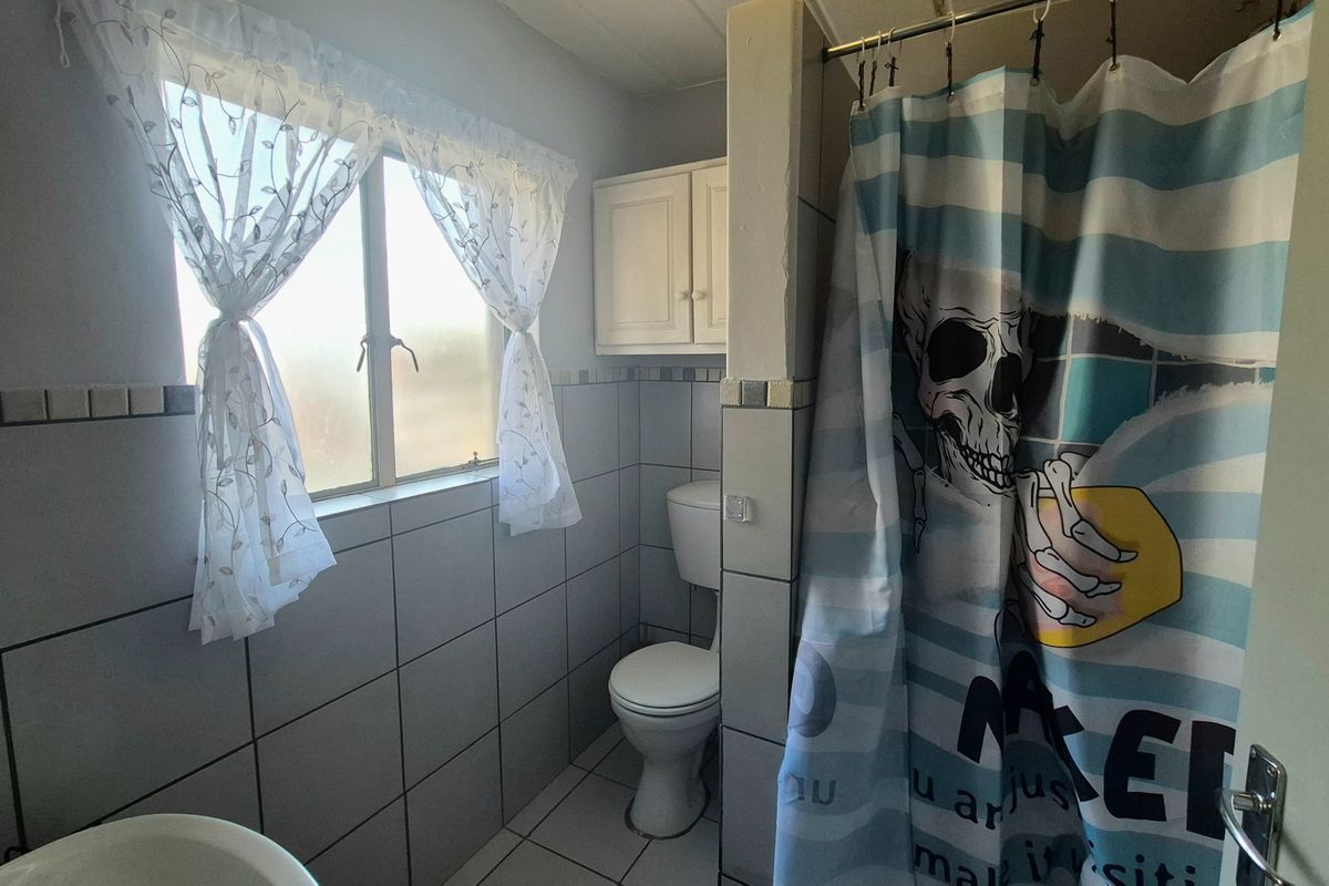 A functional bathroom featuring tiled walls and flooring, a standard toilet, and a shower area with a wall-mounted storage cabinet.