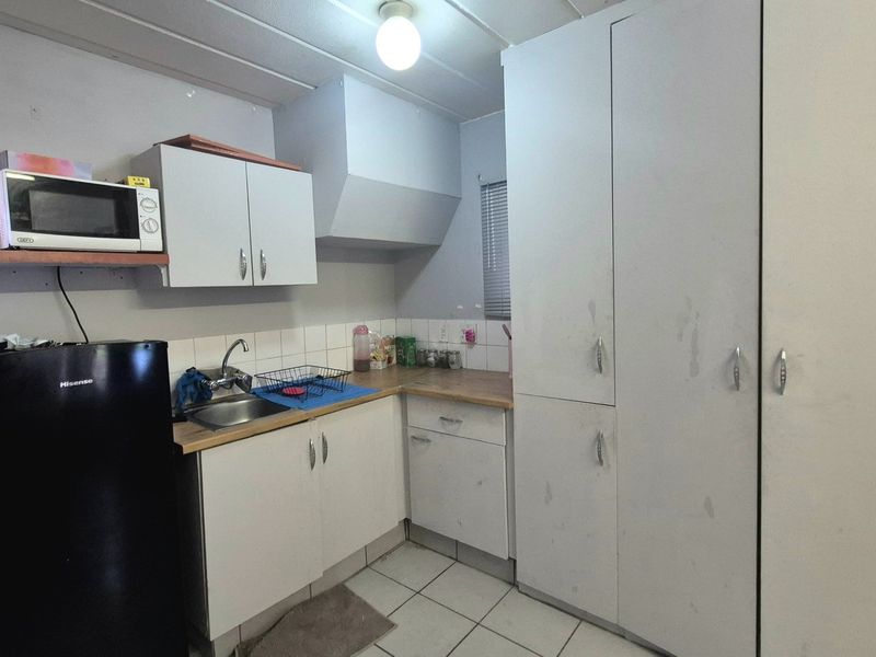 A compact kitchen featuring white built-in cabinetry, laminate countertops, a stainless steel sink, and tiled flooring, offering a functional space with potential for modernization.