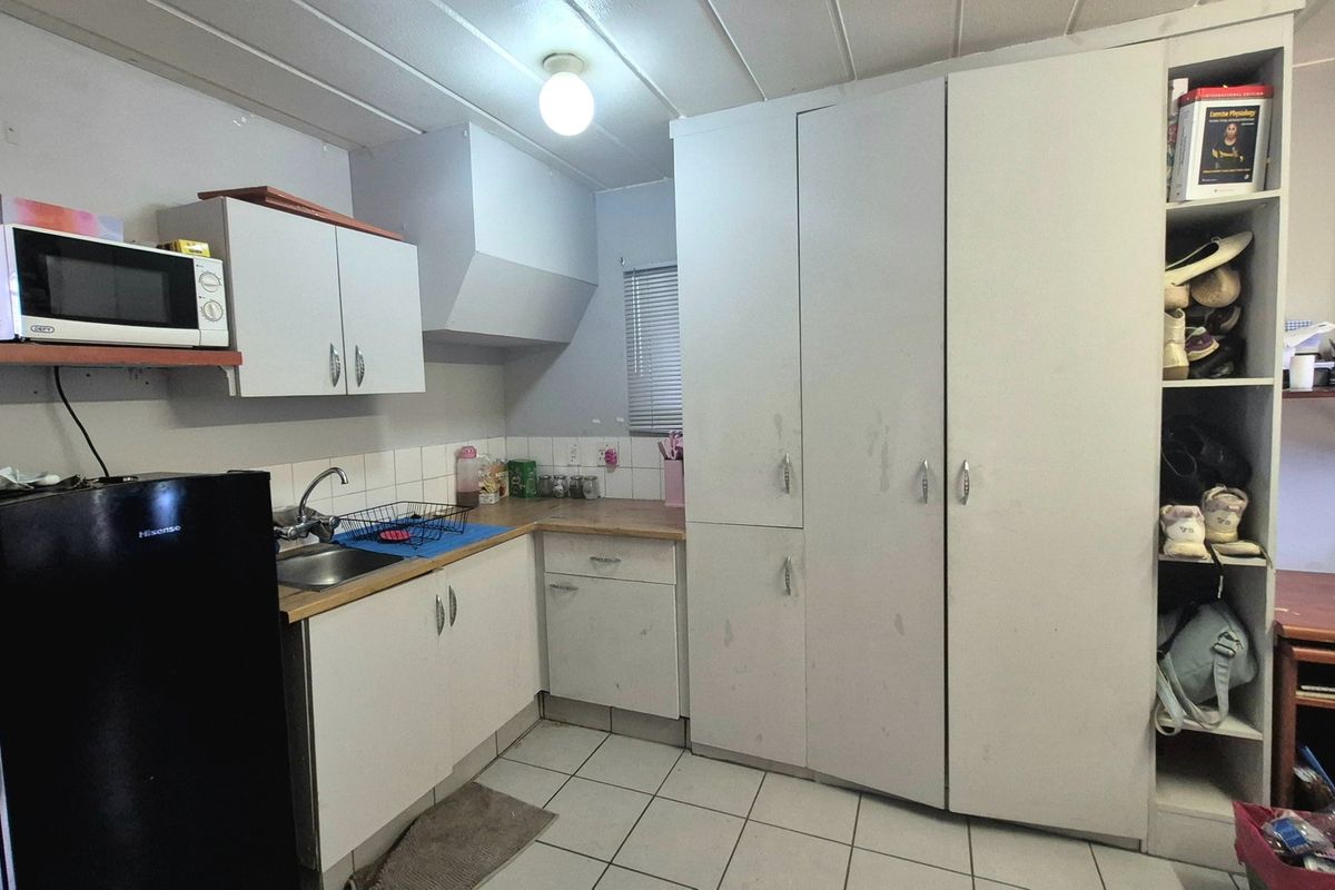 A compact kitchen featuring white built-in cabinetry, laminate countertops, a stainless steel sink, and tiled flooring, offering functional storage and preparation space.