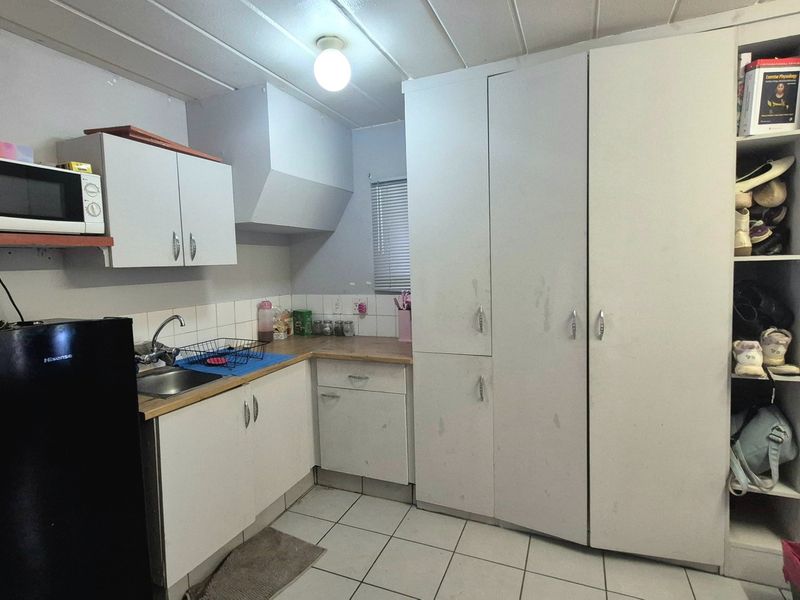 A compact kitchen featuring white built-in cabinetry, laminate countertops, a stainless steel sink, and tiled flooring, offering functional storage and preparation space.