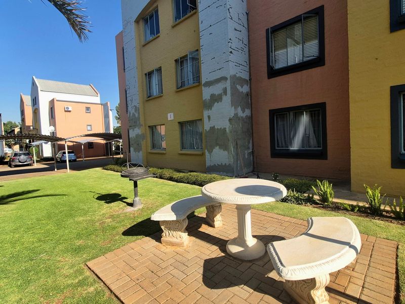 Communal garden area featuring a paved patio, fixed stone seating, and covered parking bays within the apartment complex grounds.