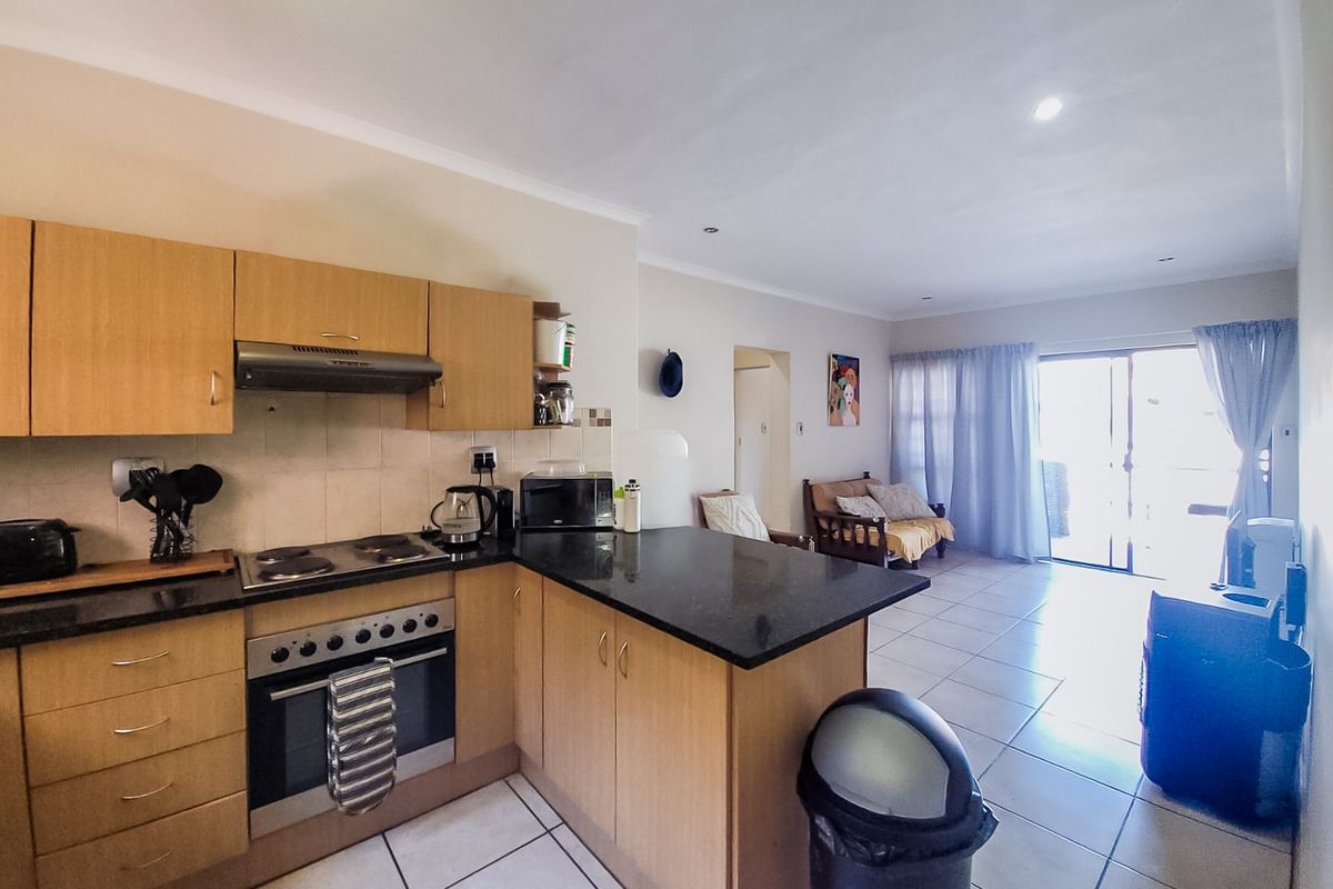 Open-plan kitchen and living area featuring light wood cabinetry, granite countertops, integrated appliances, and tiled flooring leading to a sliding door.