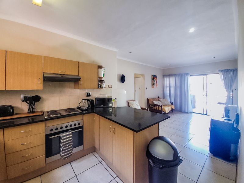Open-plan kitchen and living area featuring light wood cabinetry, granite countertops, integrated appliances, and tiled flooring leading to a sliding door.
