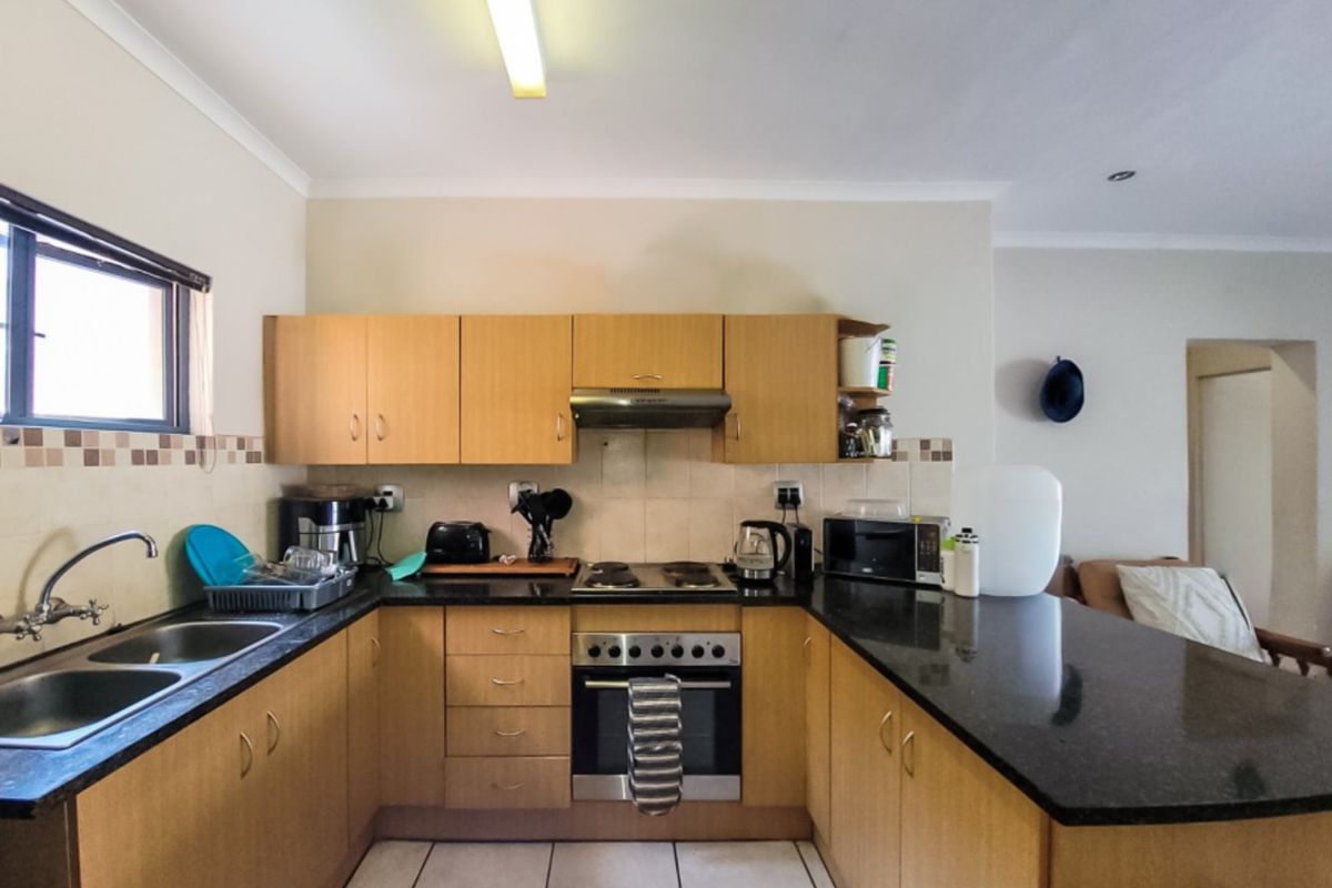 A functional kitchen featuring light wood cabinetry, dark granite countertops, a built-in oven with gas hob, and a double basin sink.