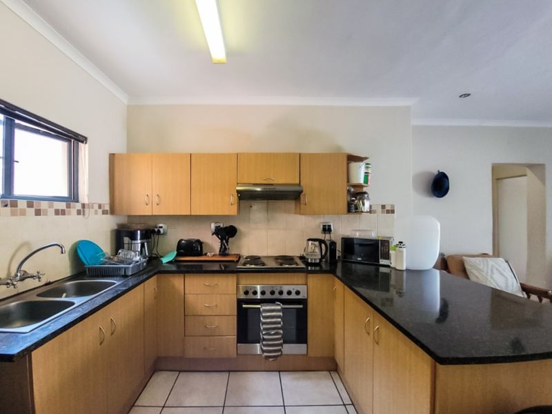 A functional kitchen featuring light wood cabinetry, dark granite countertops, a built-in oven with gas hob, and a double basin sink.