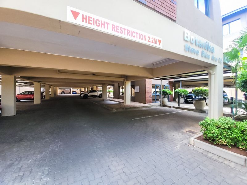 Covered parking area for the Botanika apartment complex, featuring paved flooring and concrete structural pillars with a 2.2m height restriction.