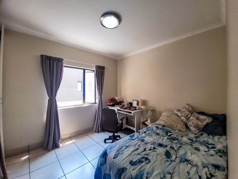 A functional bedroom featuring tiled flooring, a central ceiling light, and a casement window providing natural light.