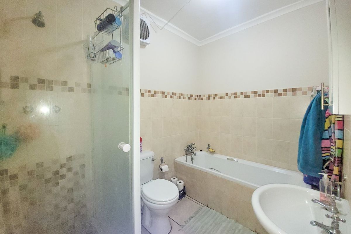 A functional bathroom featuring a separate shower enclosure, bathtub, pedestal basin, and toilet with neutral tiled walls and mosaic accent detailing.