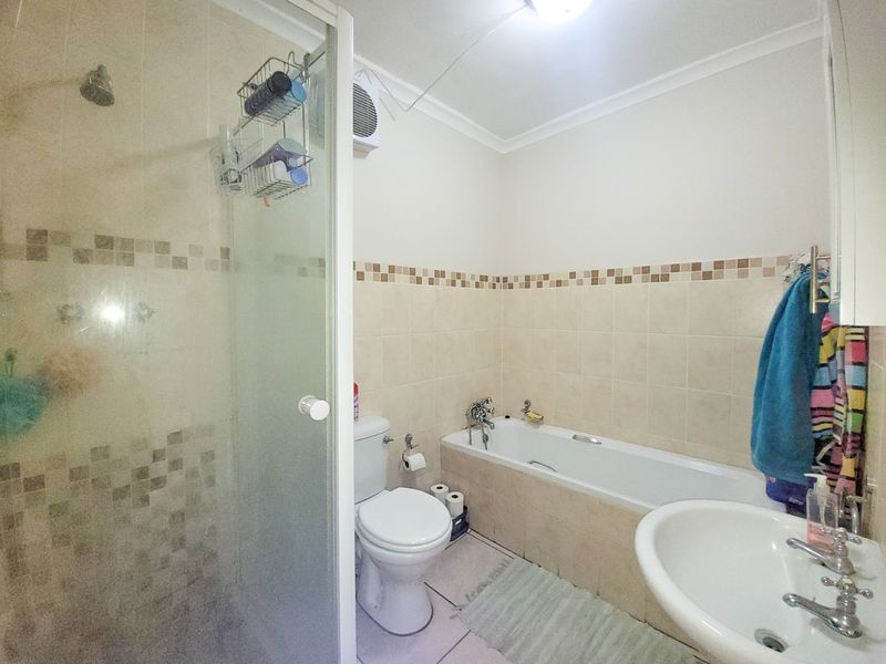 A functional bathroom featuring a separate shower enclosure, bathtub, pedestal basin, and toilet with neutral tiled walls and mosaic accent detailing.