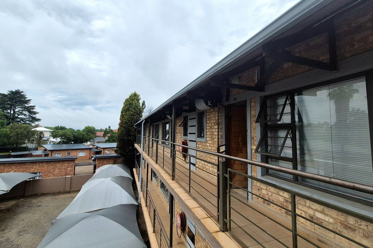 Exterior view of an apartment building featuring a brick facade, metal balcony walkways, and covered parking area below.