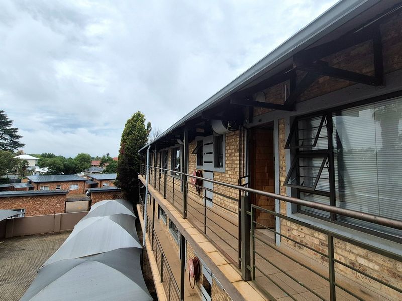 Exterior view of an apartment building featuring a brick facade, metal balcony walkways, and covered parking area below.