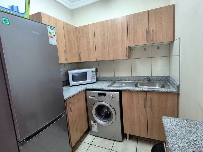 A functional laundry area featuring laminate cabinetry, granite countertops, a stainless steel sink, and tiled finishes.