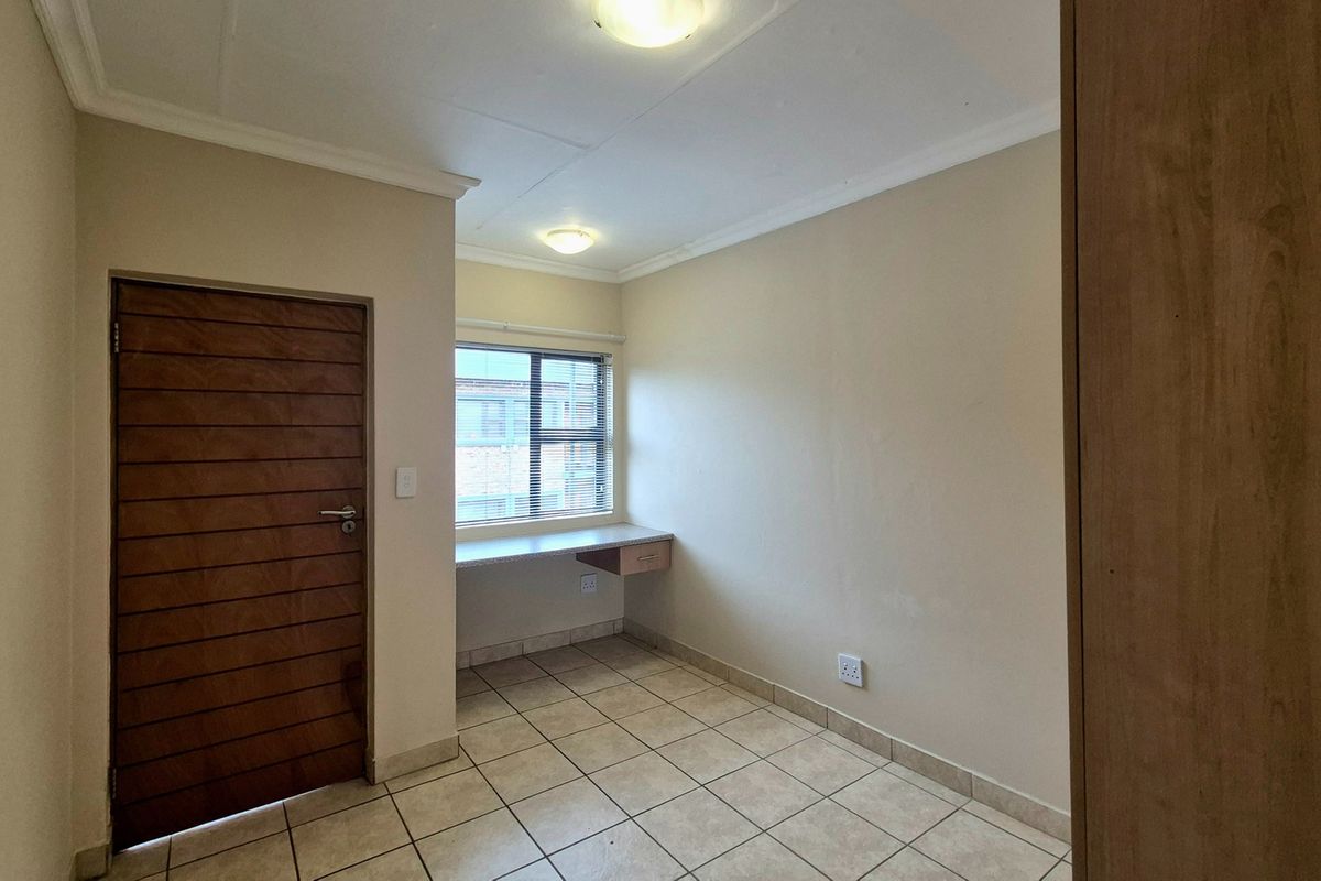 A clean, empty bedroom featuring tiled flooring, a built-in desk area, and a built-in cupboard, offering a functional space ready for personalization.