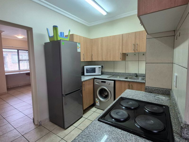Functional kitchen featuring built-in cabinetry, granite countertops, a stainless steel sink, and an electric hob with tiled backsplash and flooring.