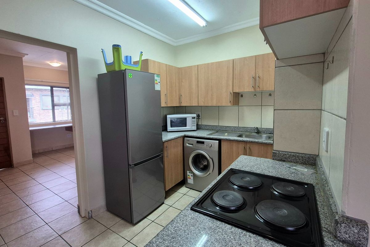 Functional kitchen featuring built-in cabinetry, granite countertops, a stainless steel sink, and an electric hob with tiled backsplash and flooring.
