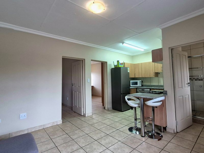 Open plan living area featuring tiled floors, a compact kitchen with built-in cabinetry, and direct access to a bathroom with a shower enclosure.