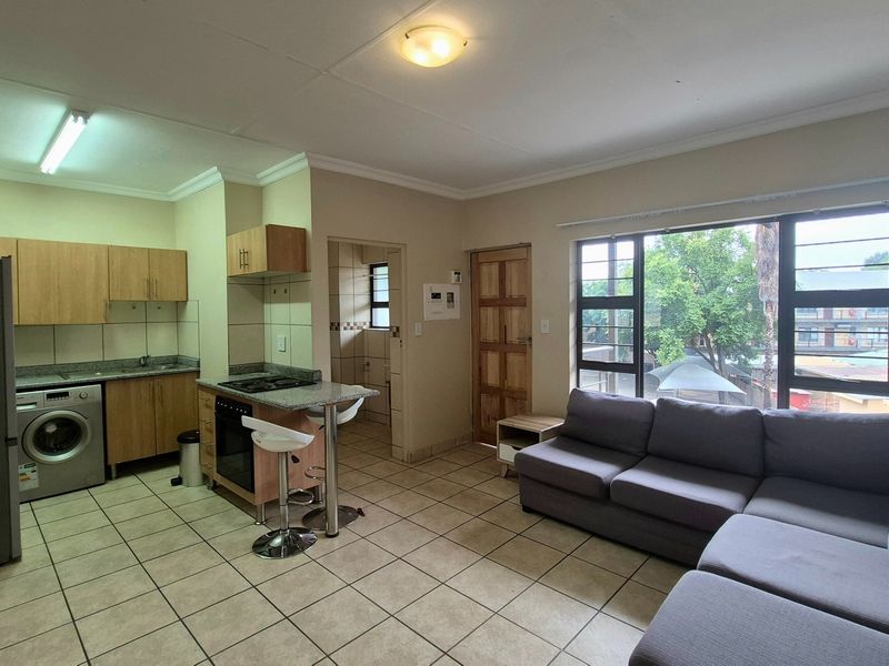 Open-plan living area featuring a functional kitchen with built-in cabinetry, granite countertops, and tiled flooring, seamlessly connected to the lounge space.