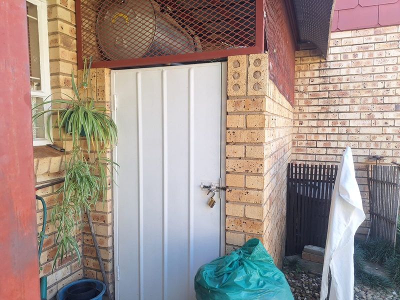 Exterior utility storage area featuring a secure metal door and brick wall construction with overhead metal mesh screening.