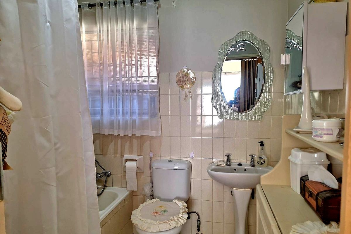 A dated bathroom featuring a pedestal basin, toilet, and bathtub with shower attachment, finished with wall tiling and a built-in medicine cabinet.