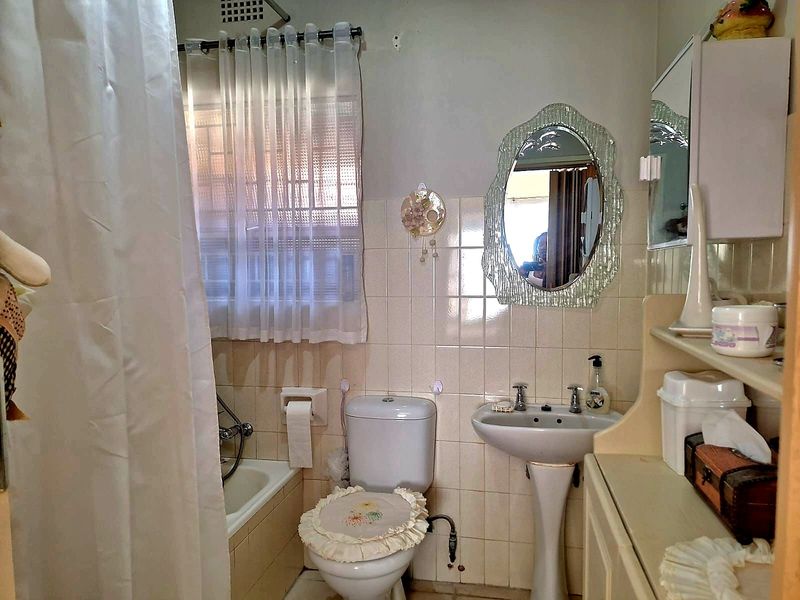 A dated bathroom featuring a pedestal basin, toilet, and bathtub with shower attachment, finished with wall tiling and a built-in medicine cabinet.