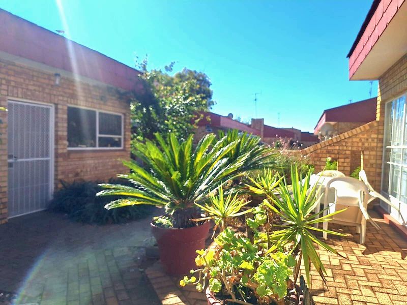 A rear exterior view of the townhouse featuring a paved patio area, brick facade, and access via a sliding glass door with a security screen.