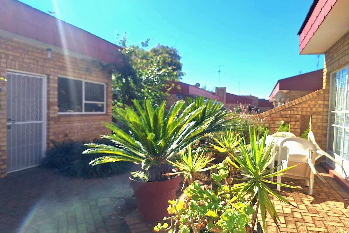 A rear exterior view of the townhouse featuring a paved patio area, brick facade, and access via a sliding glass door with a security screen.
