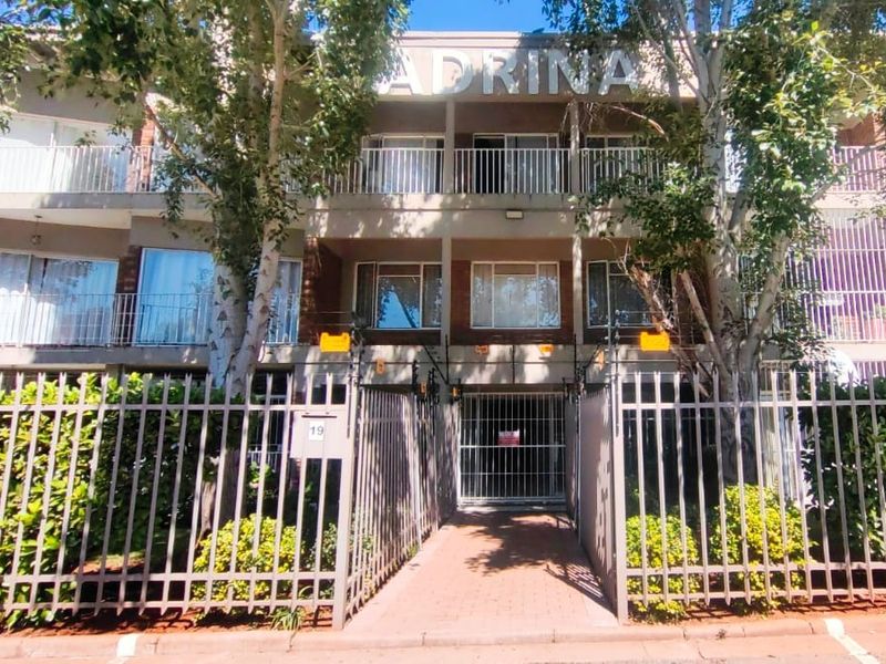 Front elevation of the Adrina apartment complex featuring secure perimeter fencing, electric security wires, and private balconies for the upper-level units.