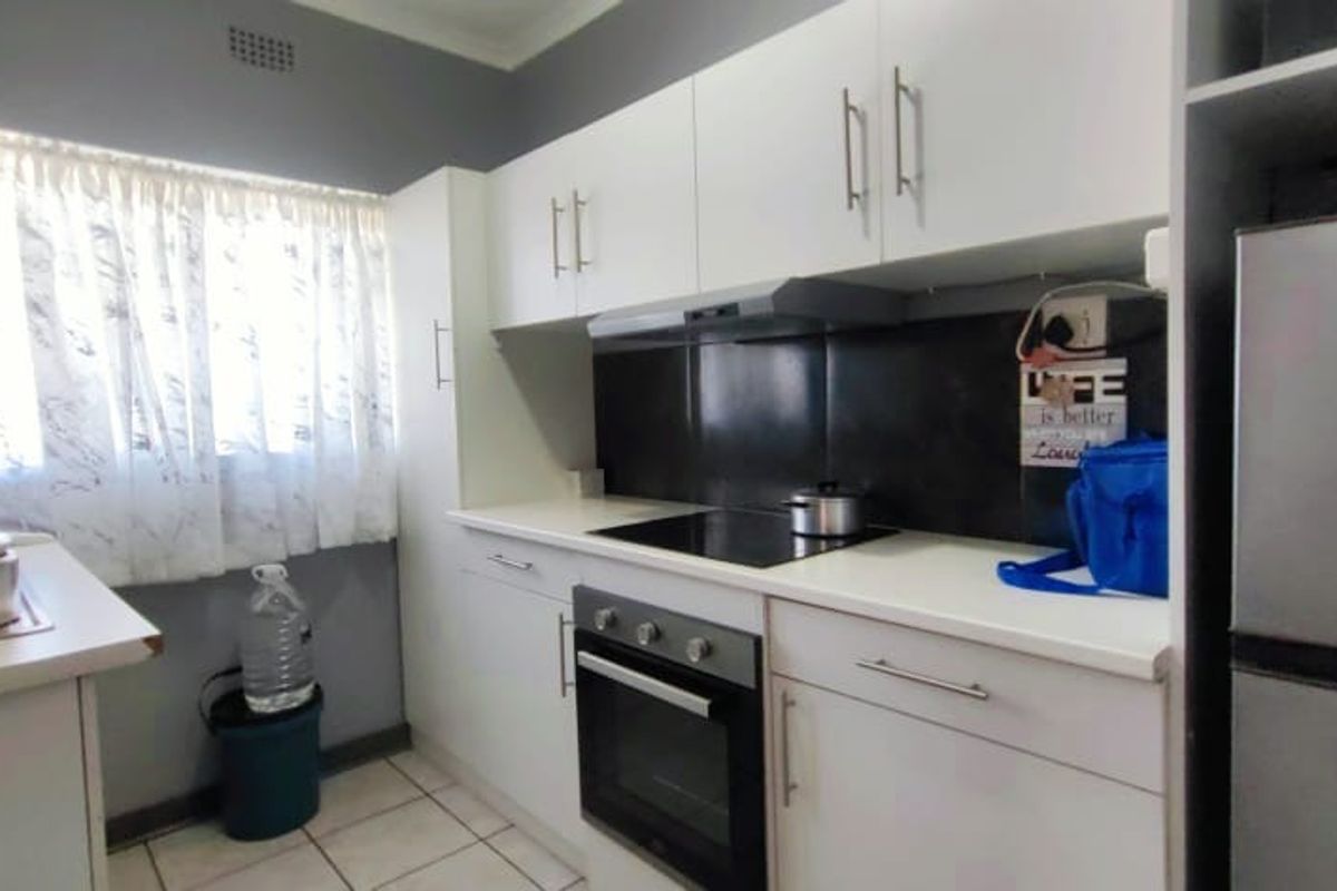 A functional kitchen featuring white cabinetry, dark splashback, integrated electric hob, oven, and extractor fan with tiled flooring.