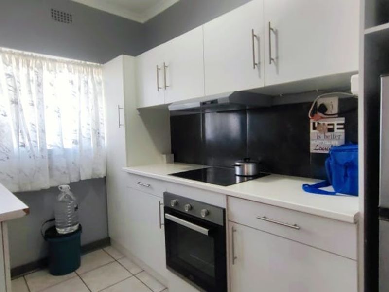 A functional kitchen featuring white cabinetry, dark splashback, integrated electric hob, oven, and extractor fan with tiled flooring.