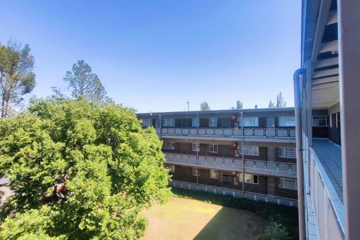 View of the apartment complex exterior, featuring a covered balcony with metal railings overlooking the communal garden and adjacent building facade.