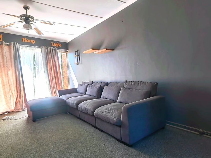 A living room featuring grey carpeting, a ceiling fan, and sliding glass doors leading to an outdoor area.