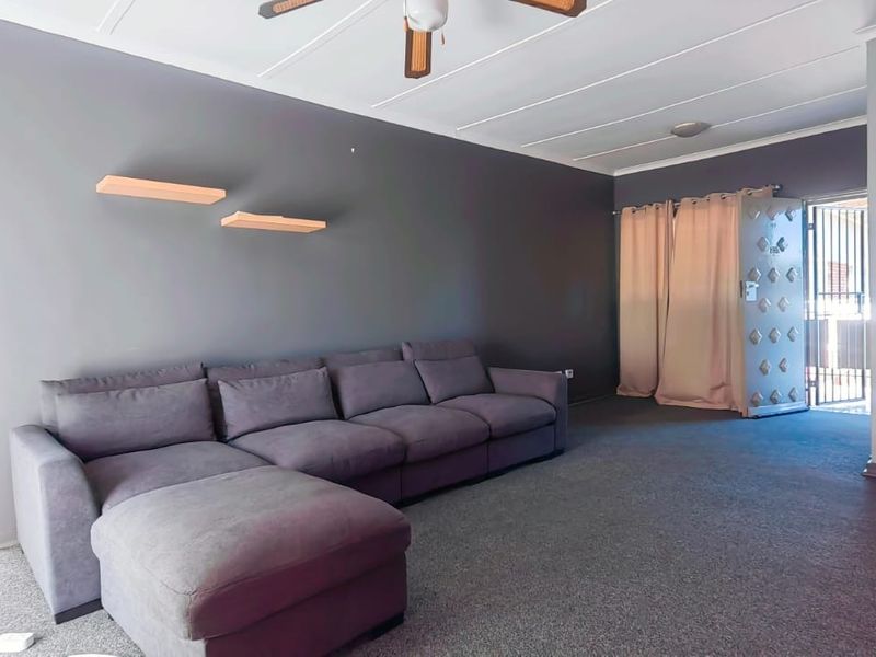 A living room featuring grey walls, carpeted flooring, a ceiling fan, and a secure metal entrance gate.