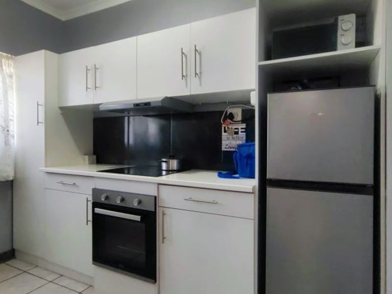 A functional kitchen featuring white cabinetry, dark splashback, built-in oven, electric hob, and tiled flooring.