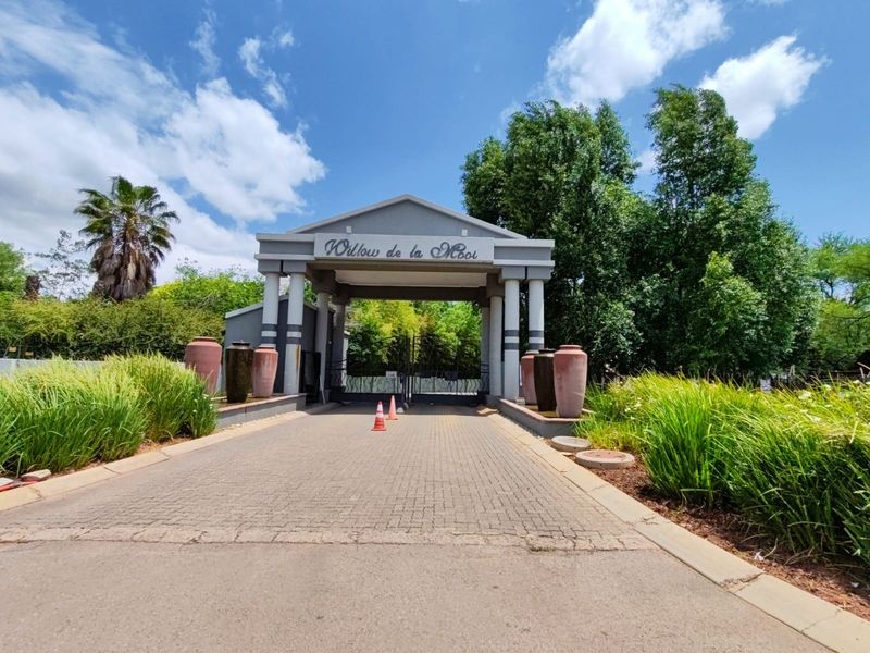 The entrance to Willow de la Mooi residential estate, featuring a paved driveway, decorative pillars, and well-maintained landscaping.