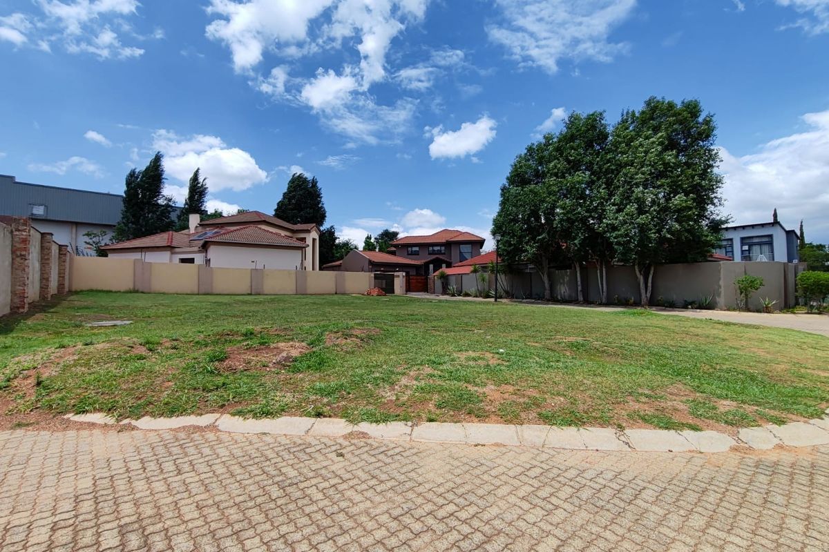 A vacant residential plot featuring a paved driveway entrance, established lawn, and perimeter walling in a developed neighborhood setting.