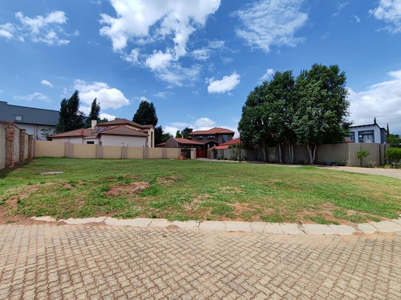 A vacant residential plot featuring a paved driveway entrance, established lawn, and perimeter walling in a developed neighborhood setting.
