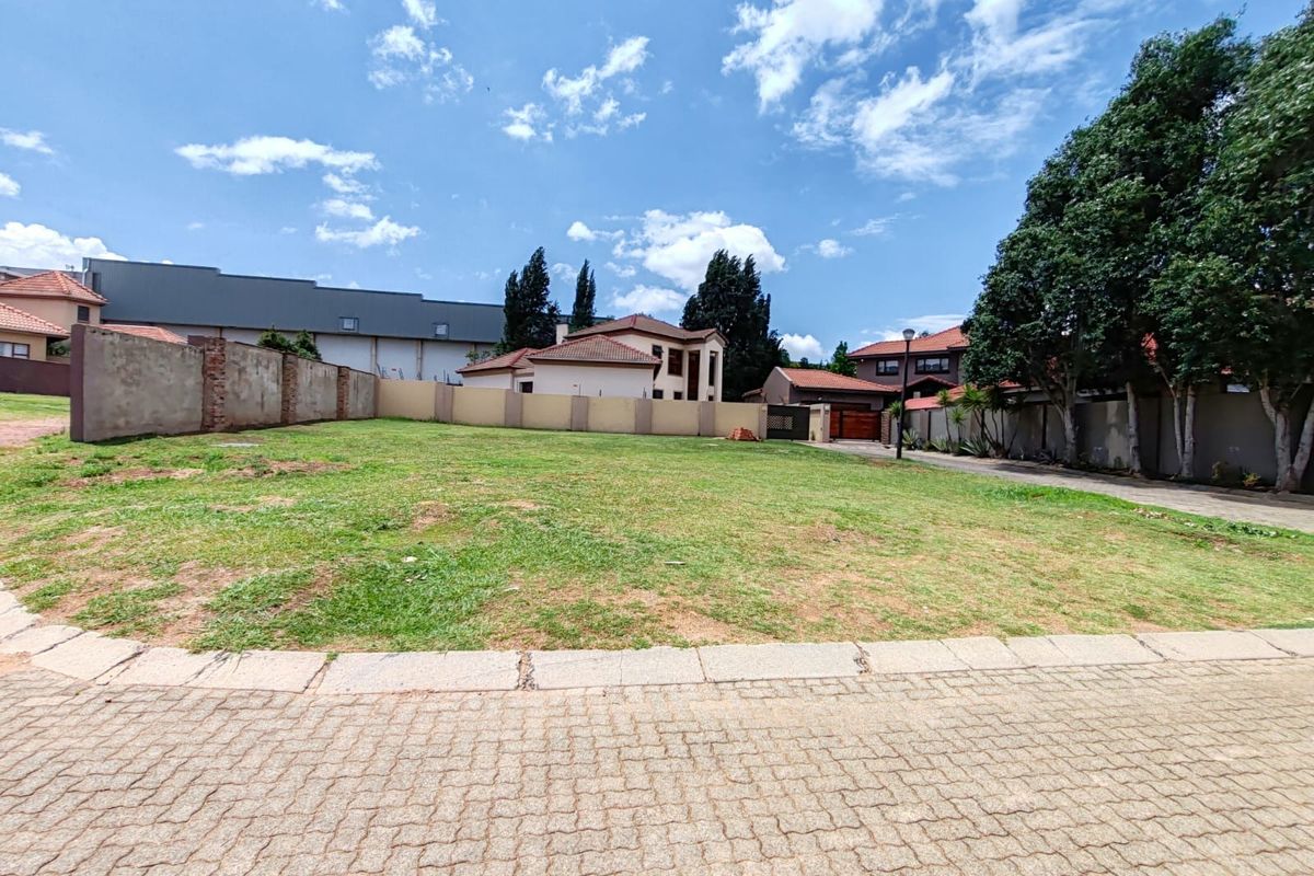 A vacant residential plot featuring a level grass lawn, perimeter boundary walls, and paved street access in a developed neighborhood.