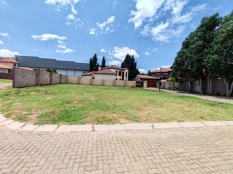 A vacant residential plot featuring a level grass lawn, perimeter boundary walls, and paved street access in a developed neighborhood.