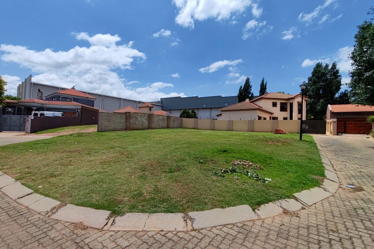 A vacant residential plot featuring a well-maintained lawn, perimeter walling, and paved access, situated within a developed residential estate.